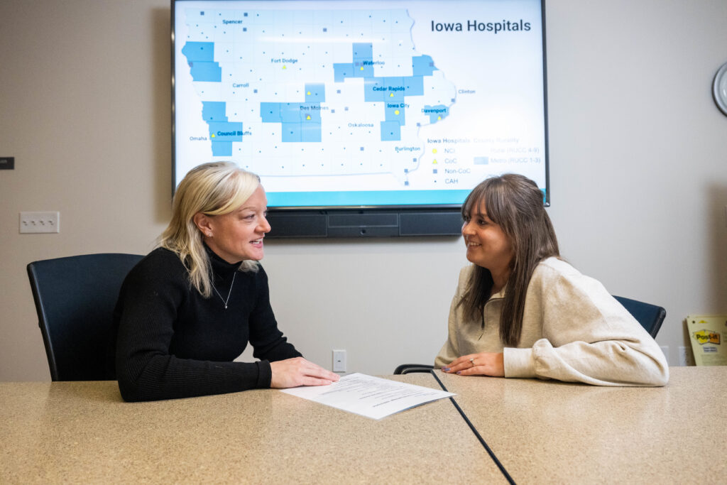 Mary Charlton (left) and Madi Whalen talking at a table with a map of Iowa hospitals in the background
