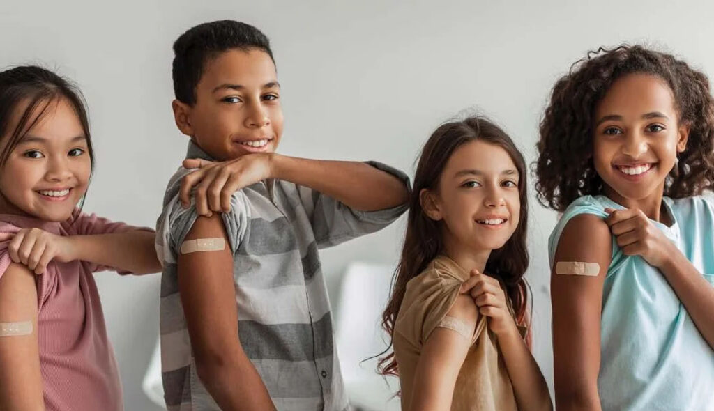 four smiling children showing bandages on their arms