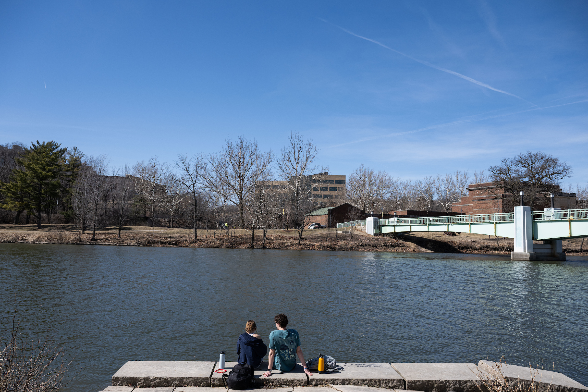 Two students gaze across the Iowa River at the College of Public Health Building in March 2025.